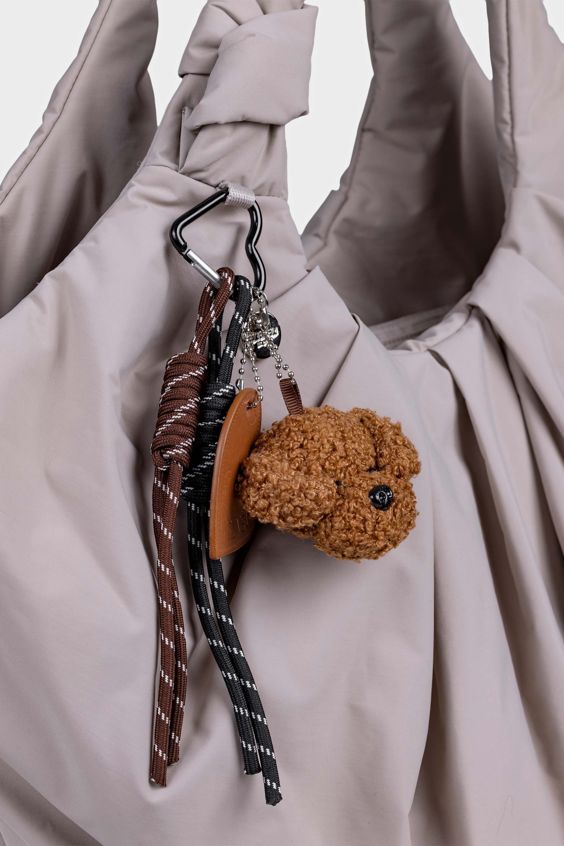 Ruskea nalle laukkukoriste, mikä on kiinnitetty beigeen laukkuun