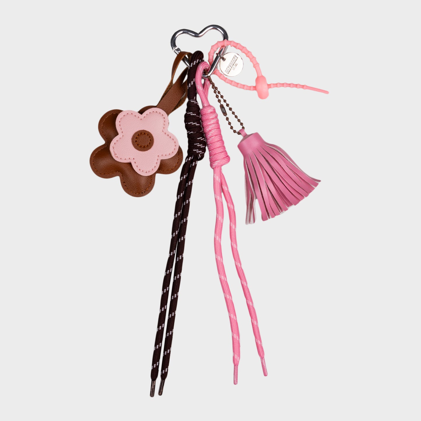 Vaaleanpunainen kukkalaukkukoru, missÀ roikkuva tupsu, kaksi nauhaa ja kaksi kukkaa.