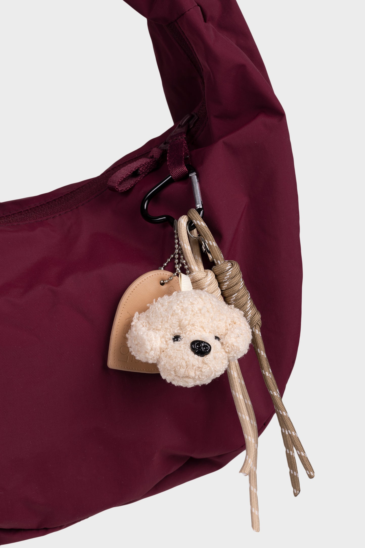 beige nalle laukkukoriste, mikä on kiinnitetty viininpunaiseen laukkuun