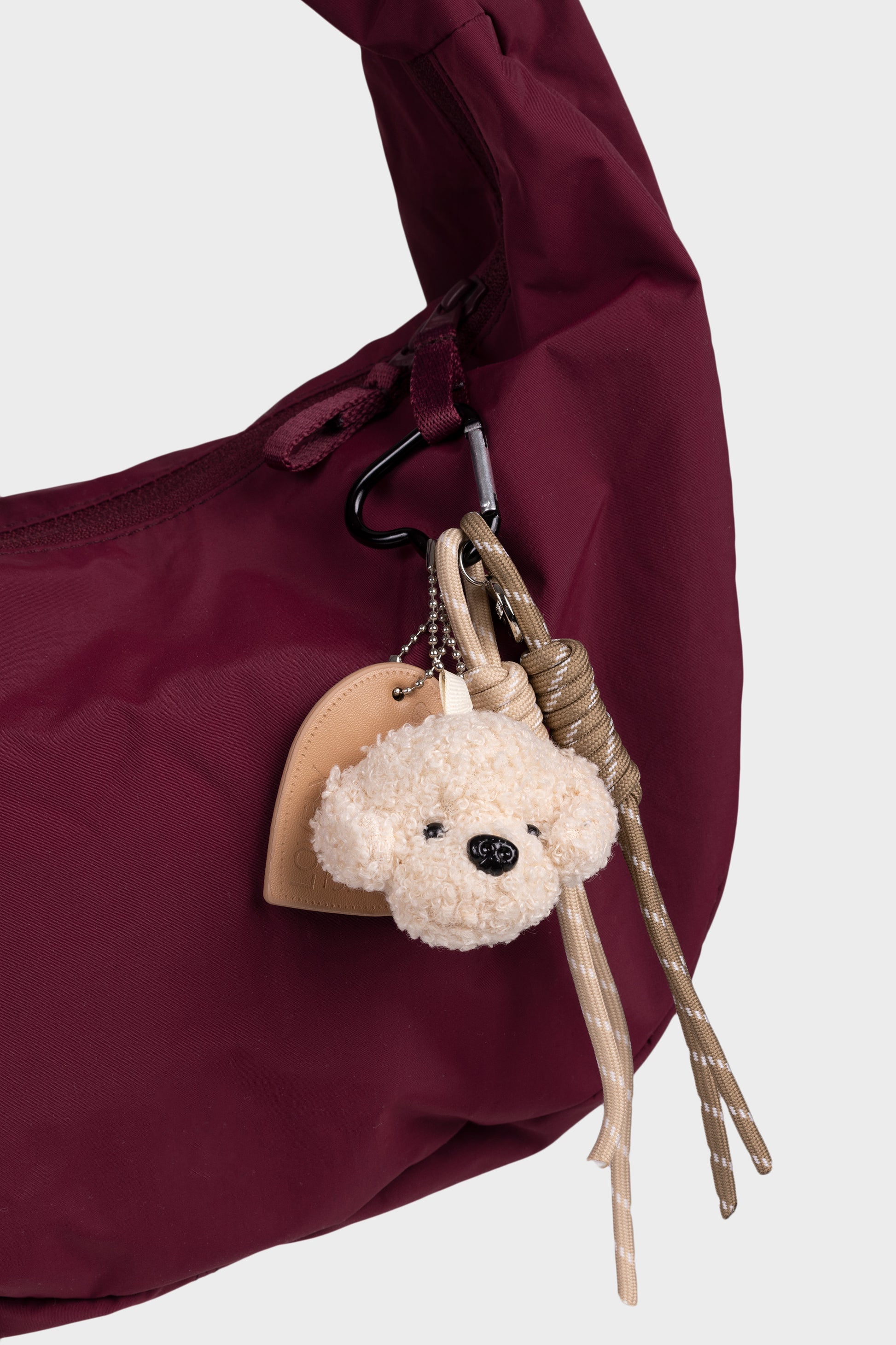 beige nalle laukkukoriste, mikä on kiinnitetty viininpunaiseen laukkuun