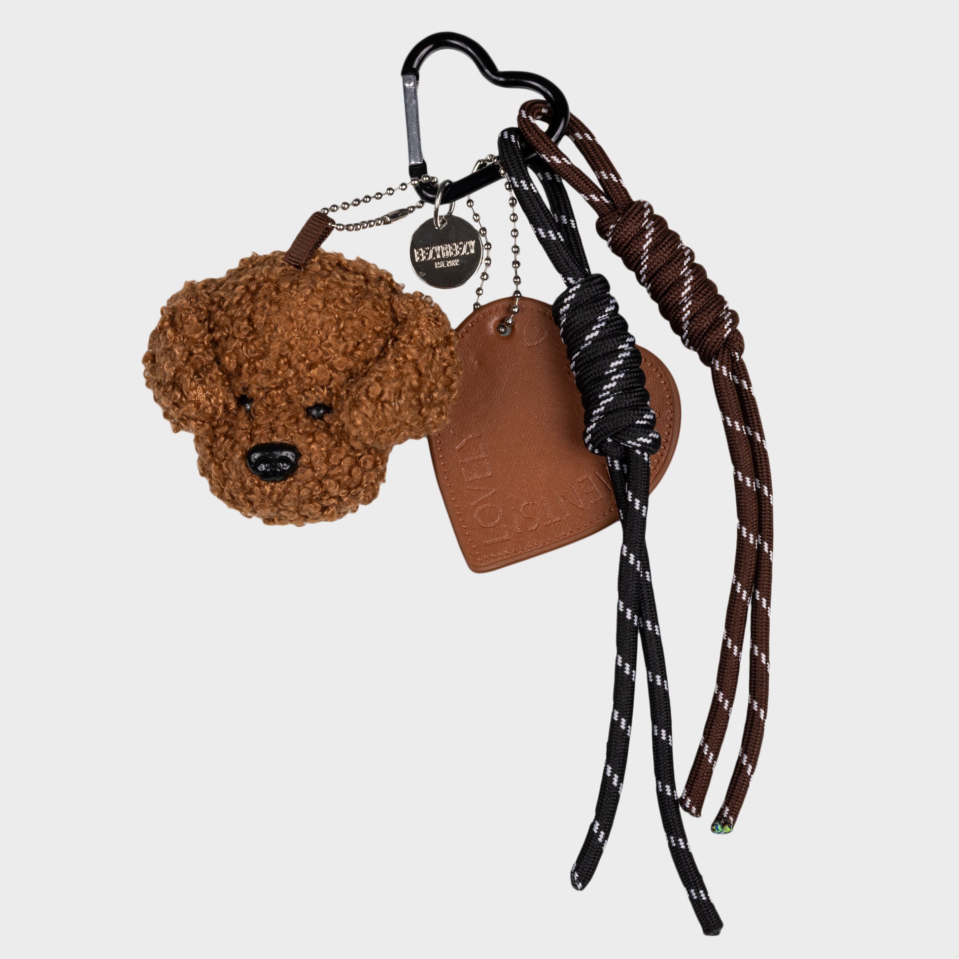 Ruskea nalle laukkukoriste, missä lisänä myös nahkajäljitelmä sydän ja roikkuvat nauhat 