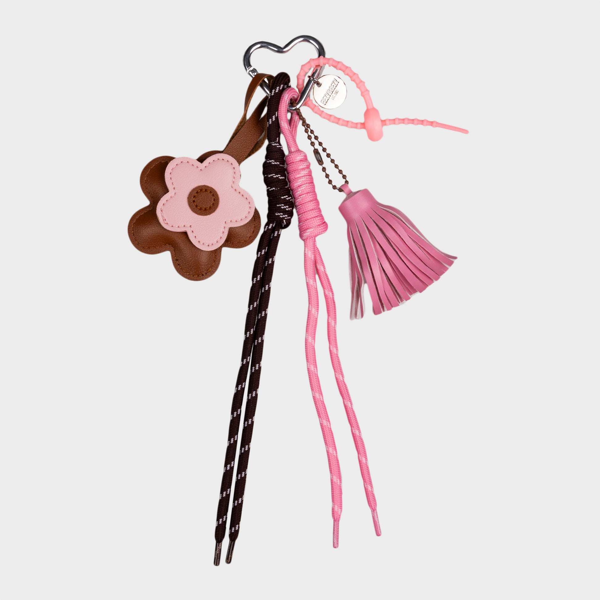 Vaaleanpunainen kukkalaukkukoru, missä roikkuva tupsu, kaksi nauhaa ja kaksi kukkaa.